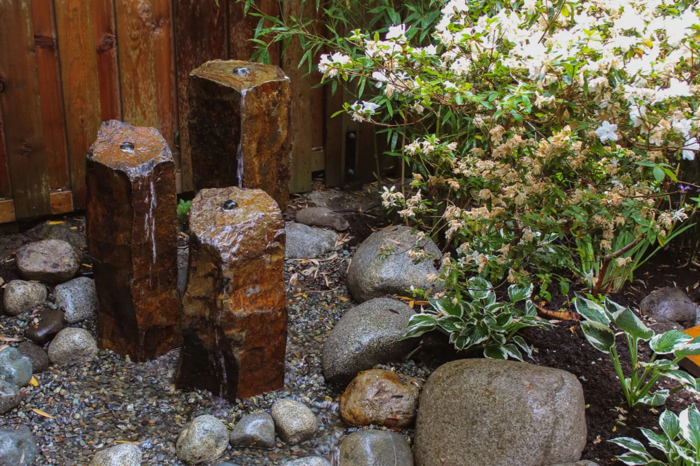 Basalt column fountains running over river stone in a planted Victoria courtyard.