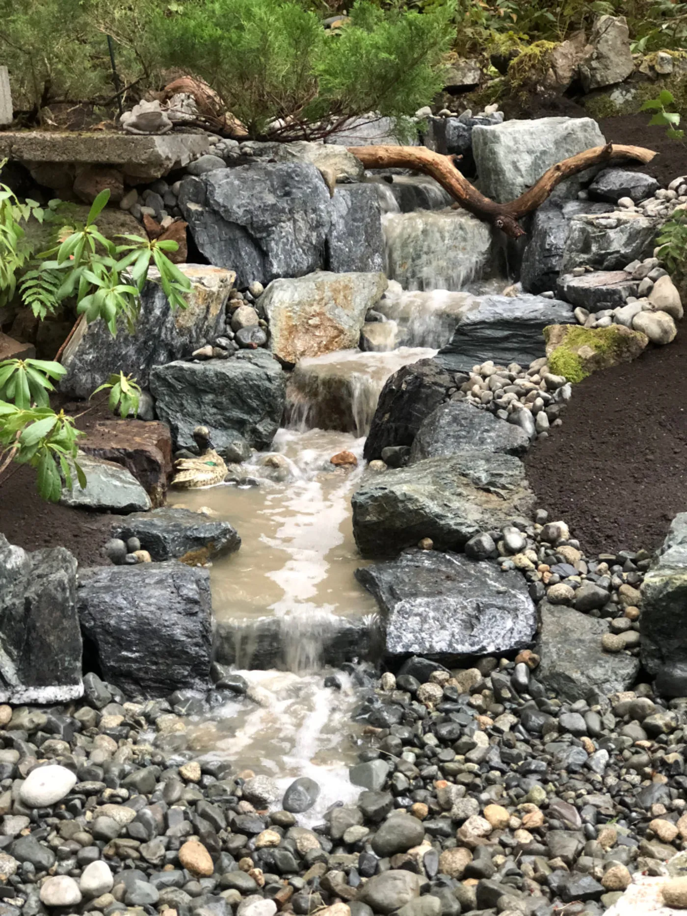Water running over stacked stone into a gravel bed on an Oxbow pondless waterfall.